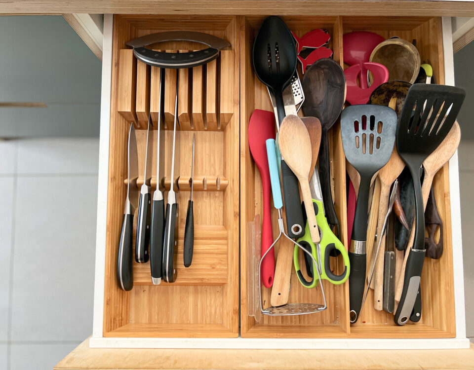 Overhead view color image depicting the interior of an open drawer in a domestic kitchen. The drawer contains a large amount of kitchen cutlery, including silver knives, forks and spoons as well as other kitchen apparatus including brushes and bread clips. The drawer is divided up neatly into multiple compartments. Room for copy space.